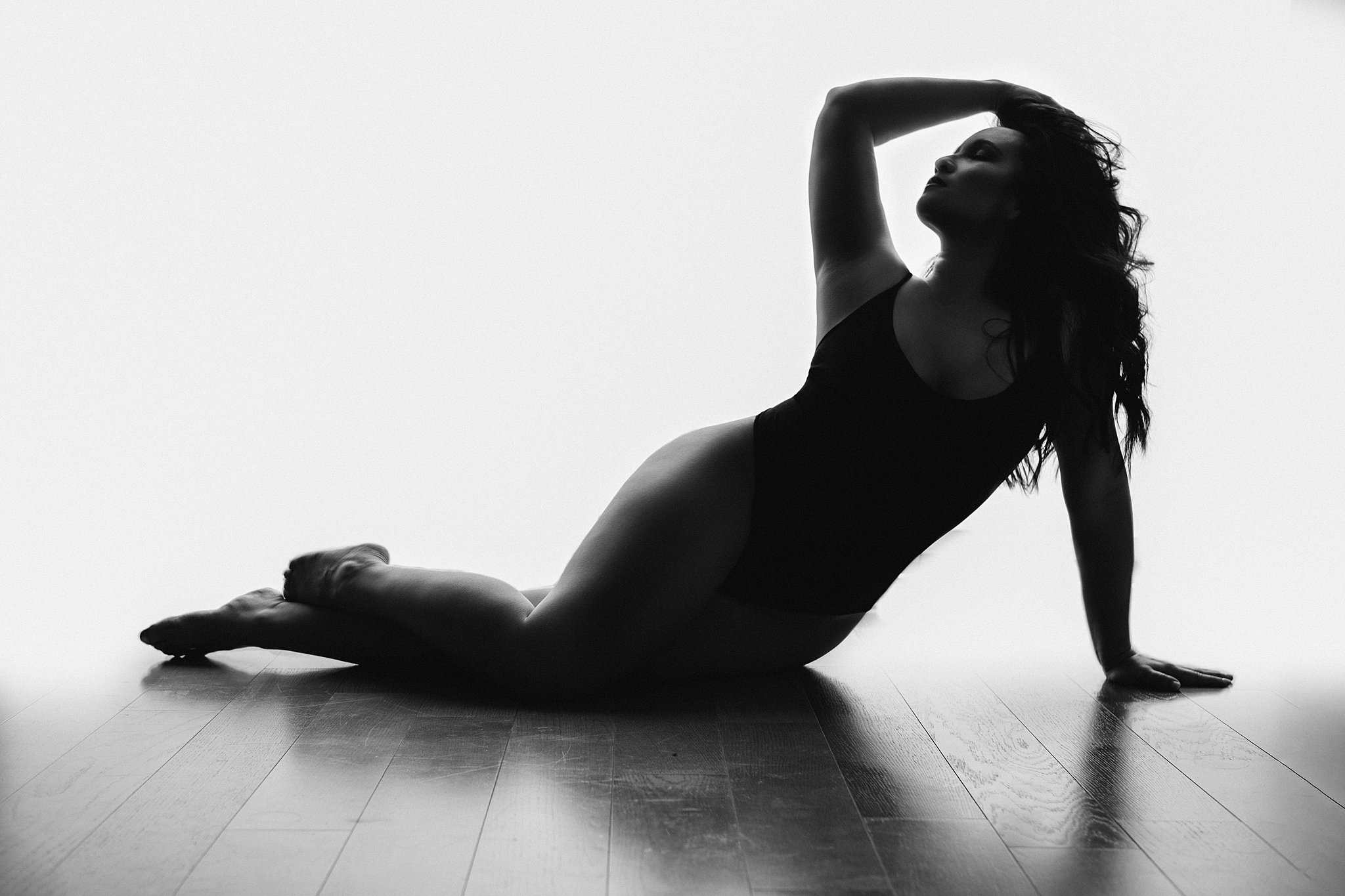 Silhouette of a woman laying on a hardwood floor in front of a window with a hand running through her hair spas in alpharetta